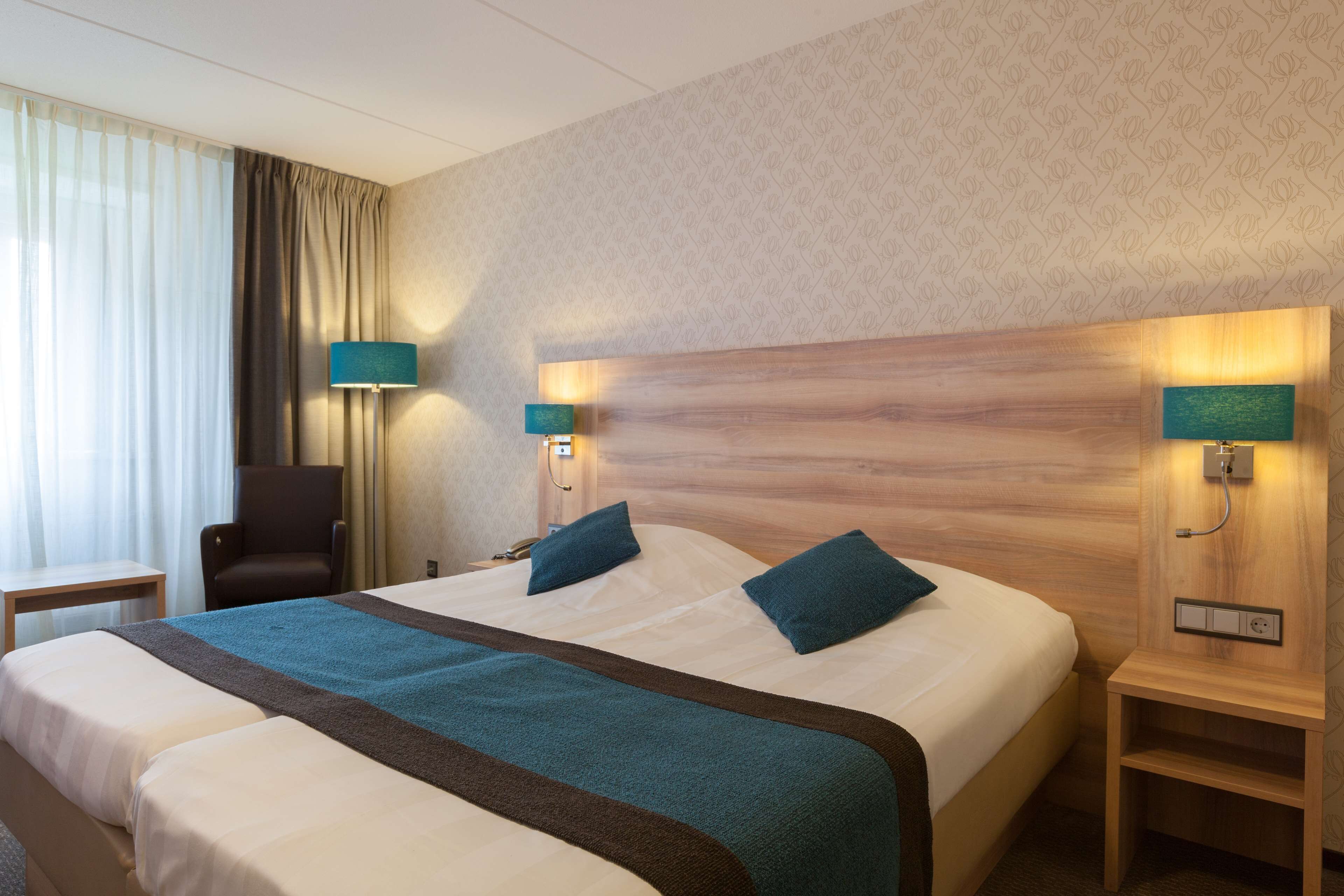 Een hotelkamer met een groot bed, twee nachtkastjes, een stoel en een bureau.