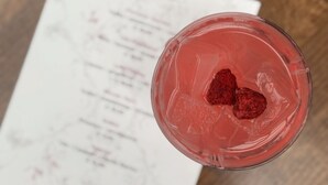 A glass with a pink drink and two strawberries on ice, placed on a wooden table with a menu in the background. - Best Western Hotel Baars (Harderwijk)