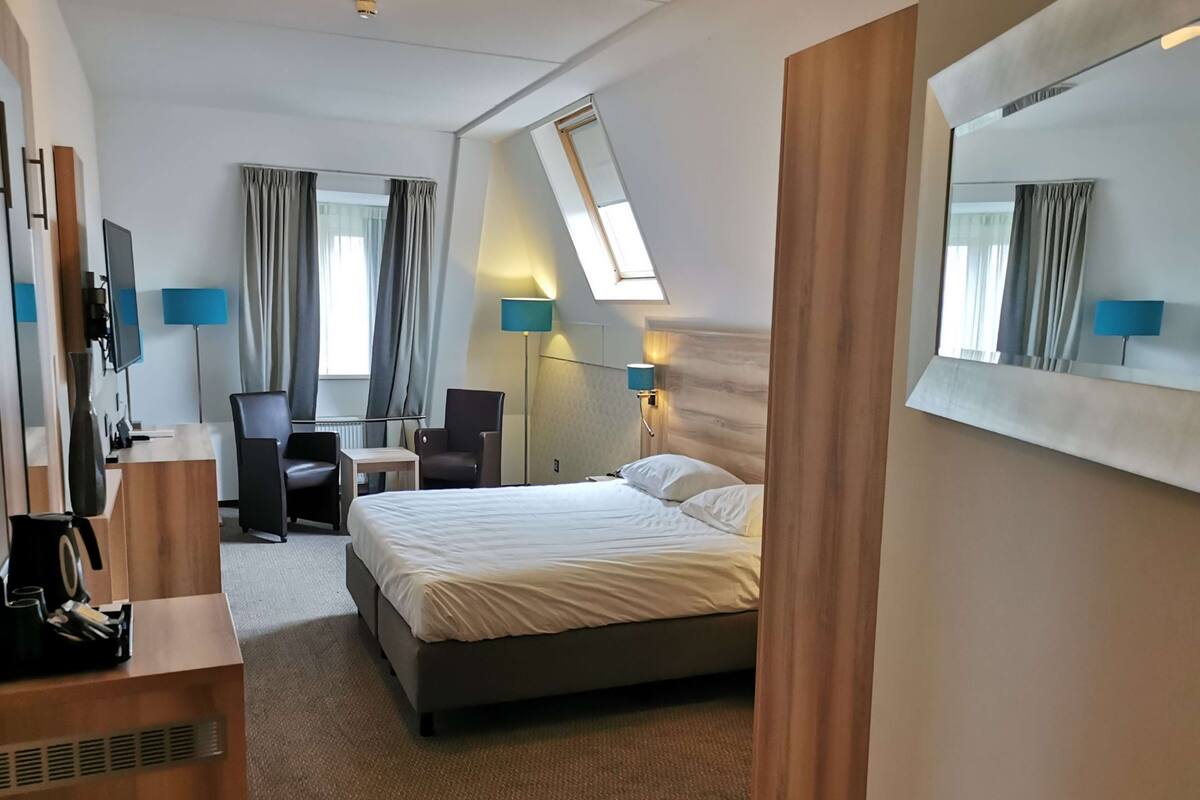 Habitación de hotel con cama, escritorio, silla y un espejo grande.