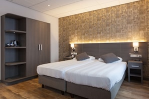 Una habitación de hotel moderna con una cama grande, un armario y una mesita de noche con lámpara.