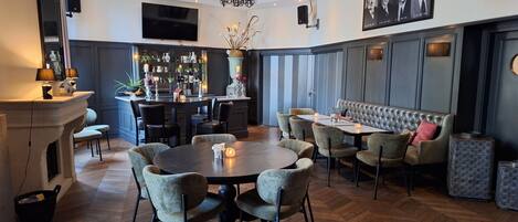 A modern dining area with a round table, cushioned chairs, a bar area with shelves, and a large television.