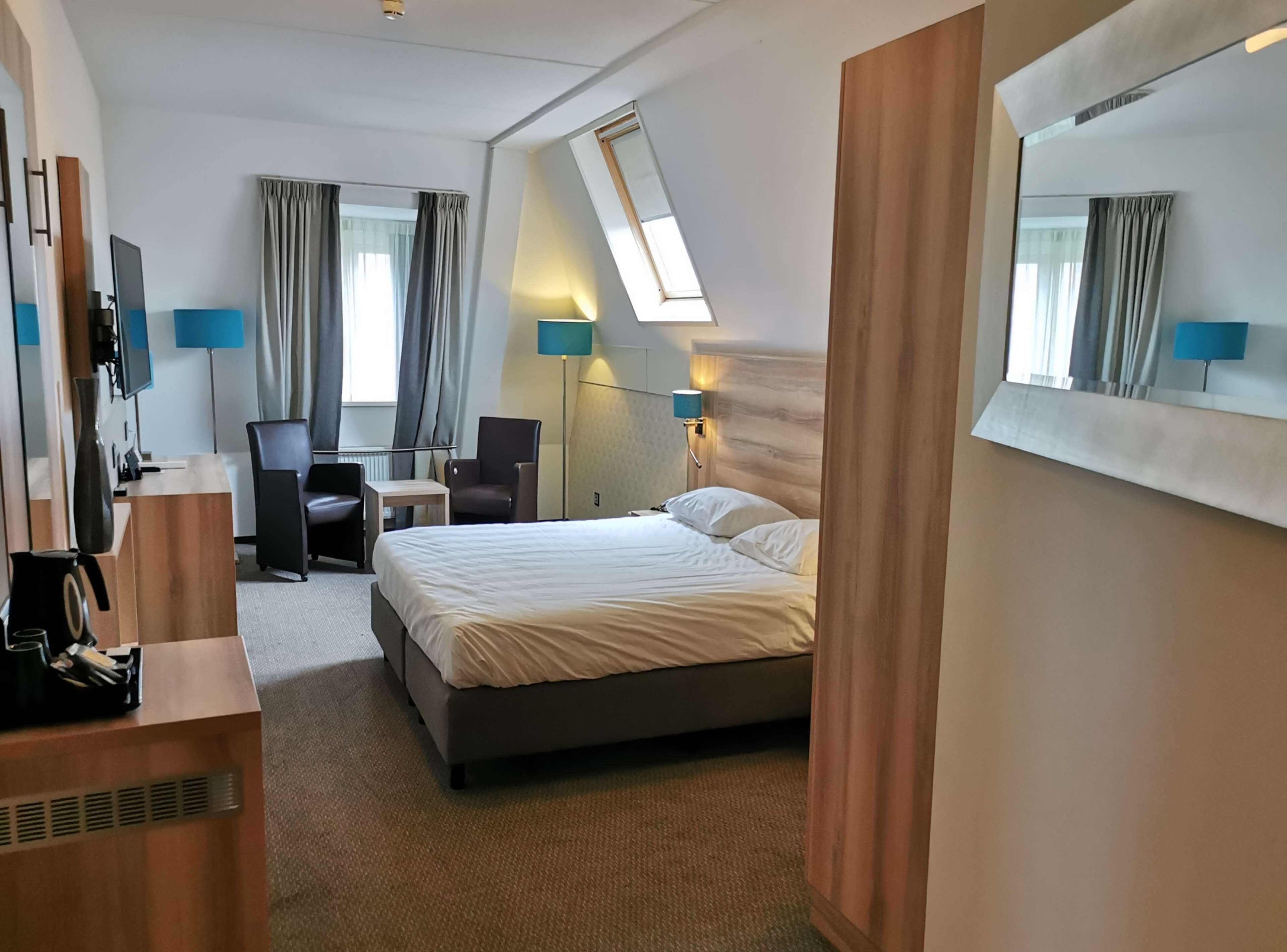 Une chambre d’hôtel avec un lit, un bureau, une chaise et un grand miroir.