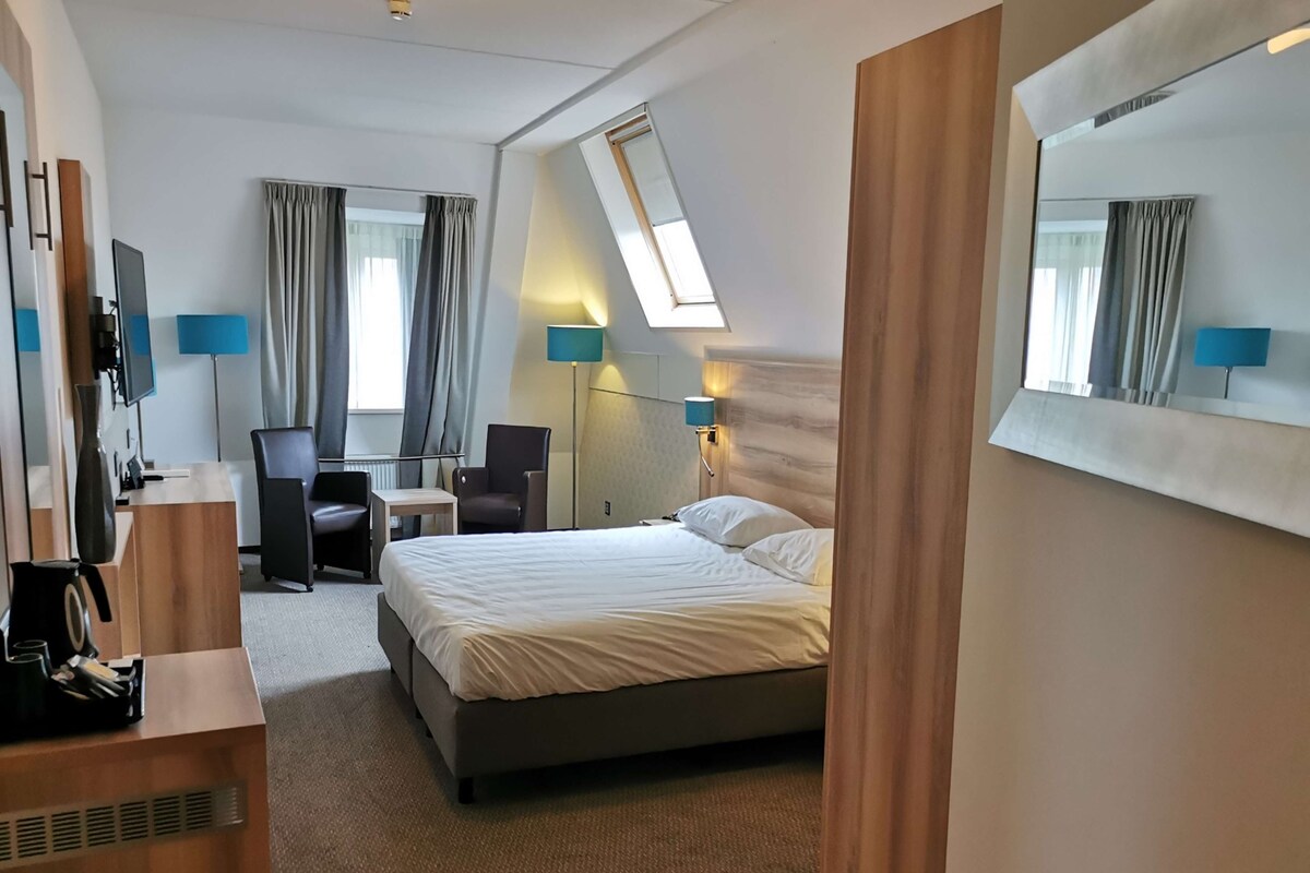 Une chambre d’hôtel avec un lit, un bureau, une chaise et un grand miroir.