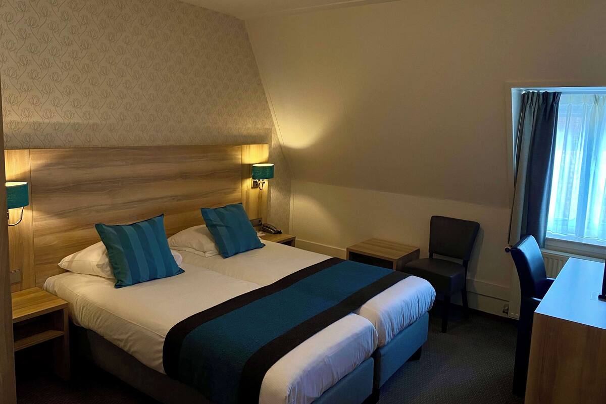 Habitación de hotel con una cama grande, dos mesitas de noche, un escritorio y una silla.