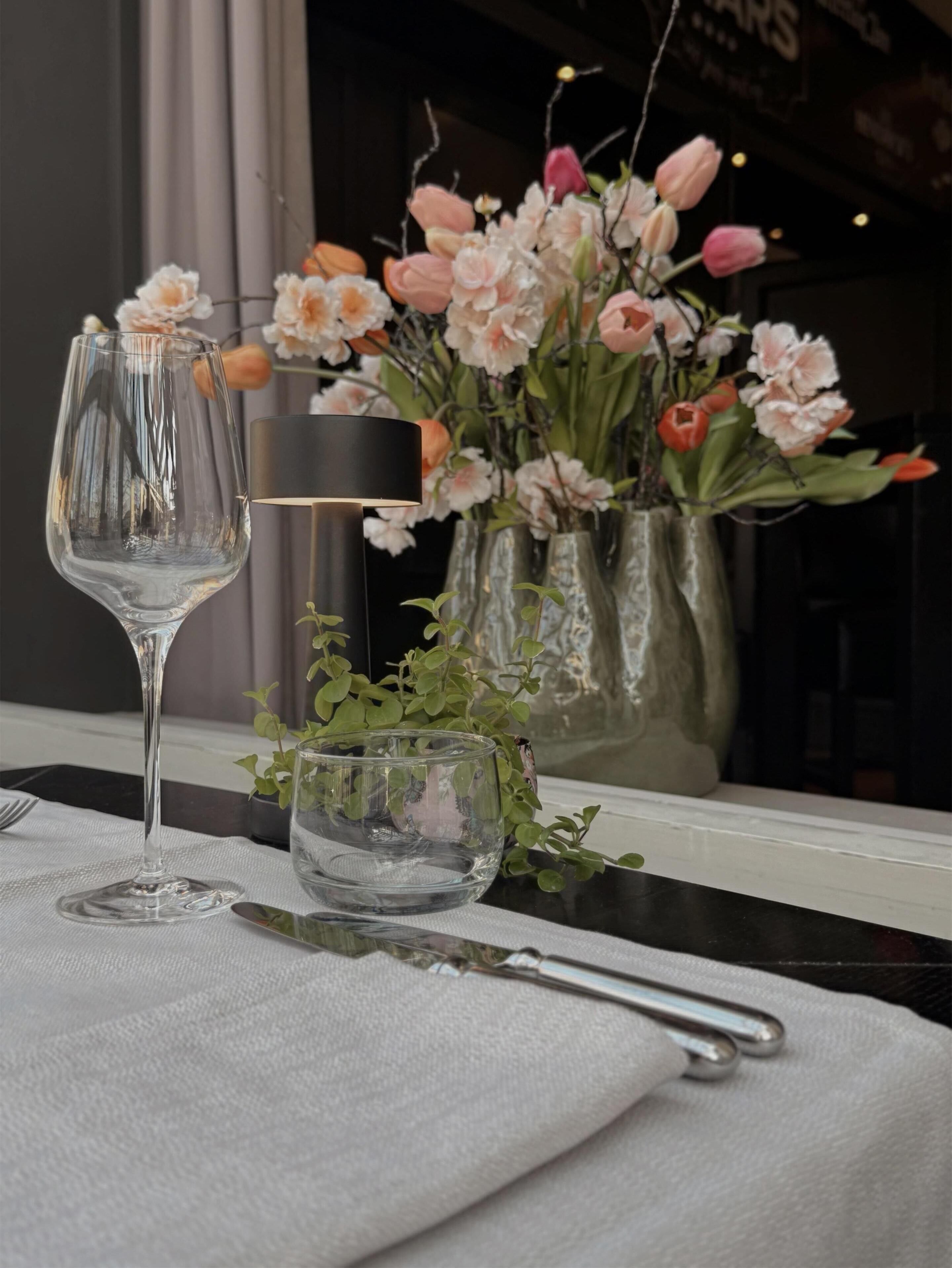 Una mesa de comedor con una copa de vino, un cuenco pequeño y un florero con flores.