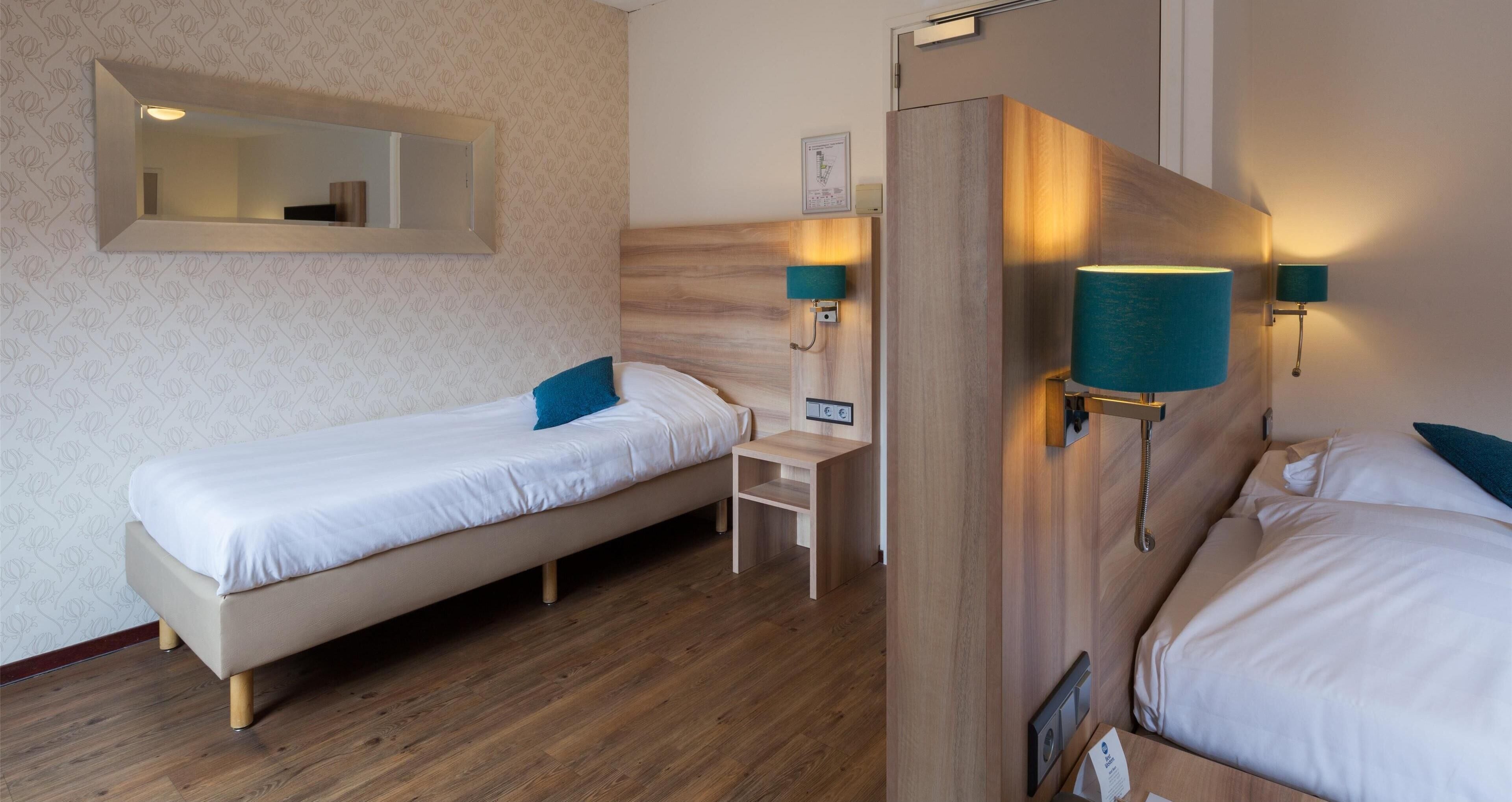 Et hotelværelse med to enkeltsenge, et træhovedgærde, et lille skrivebord og to vægmonterede lamper.