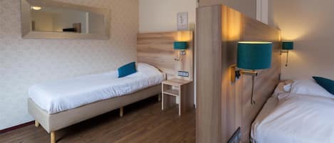 Una habitación de hotel con dos camas individuales, un cabecero de madera, un escritorio pequeño y dos lámparas de pared.