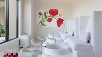 A modern spa room with a large window, white furniture, and a painting of red flowers on the wall.