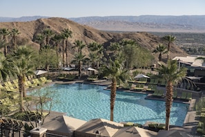 A pool area with lounge chairs and palm trees, surrounded by mountains.
