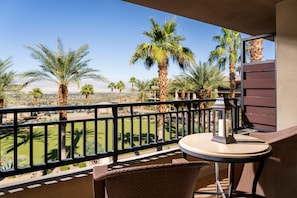 A balcony with wicker furniture, a table, and a lantern. Palm trees and a golf course are visible in the background.