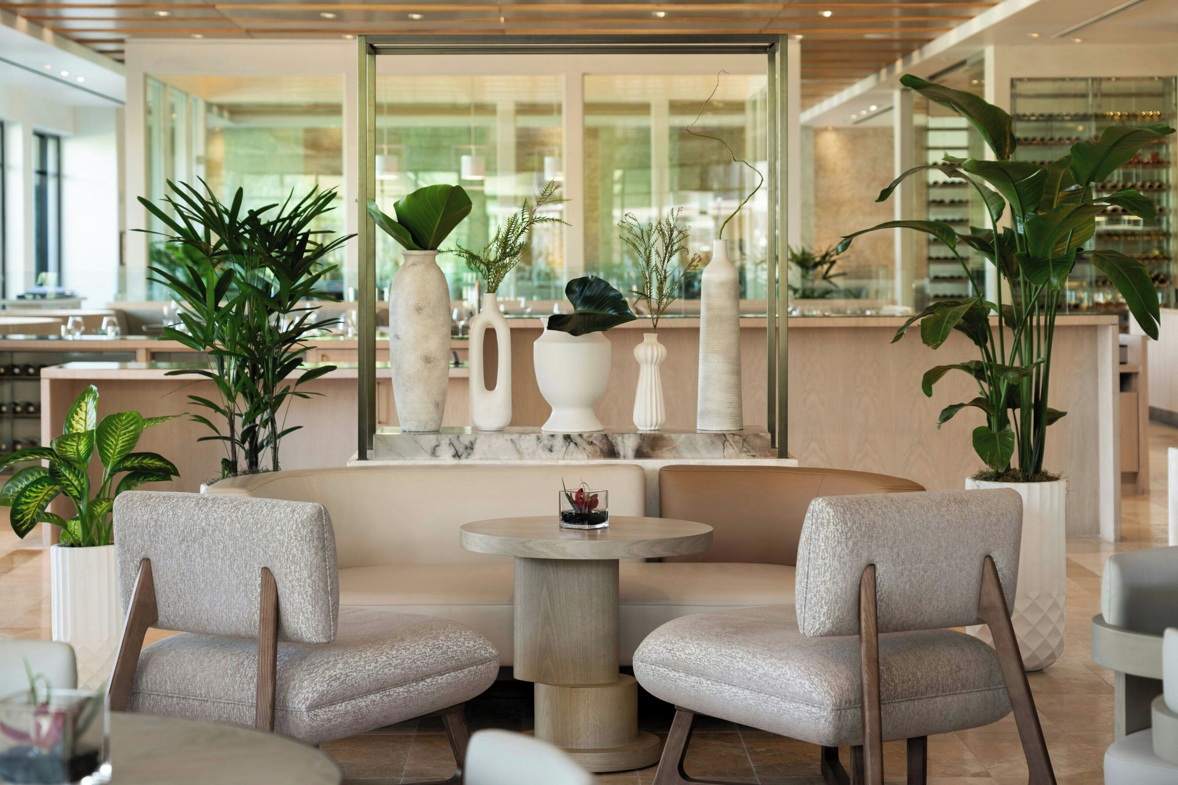 A modern hotel lobby with seating areas, large windows, and indoor plants.