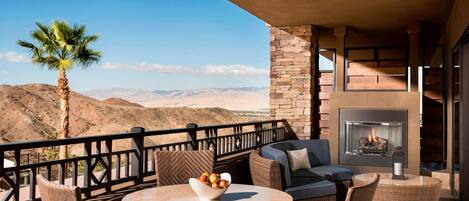 A balcony with wicker furniture, a bowl of fruit, and a fireplace.