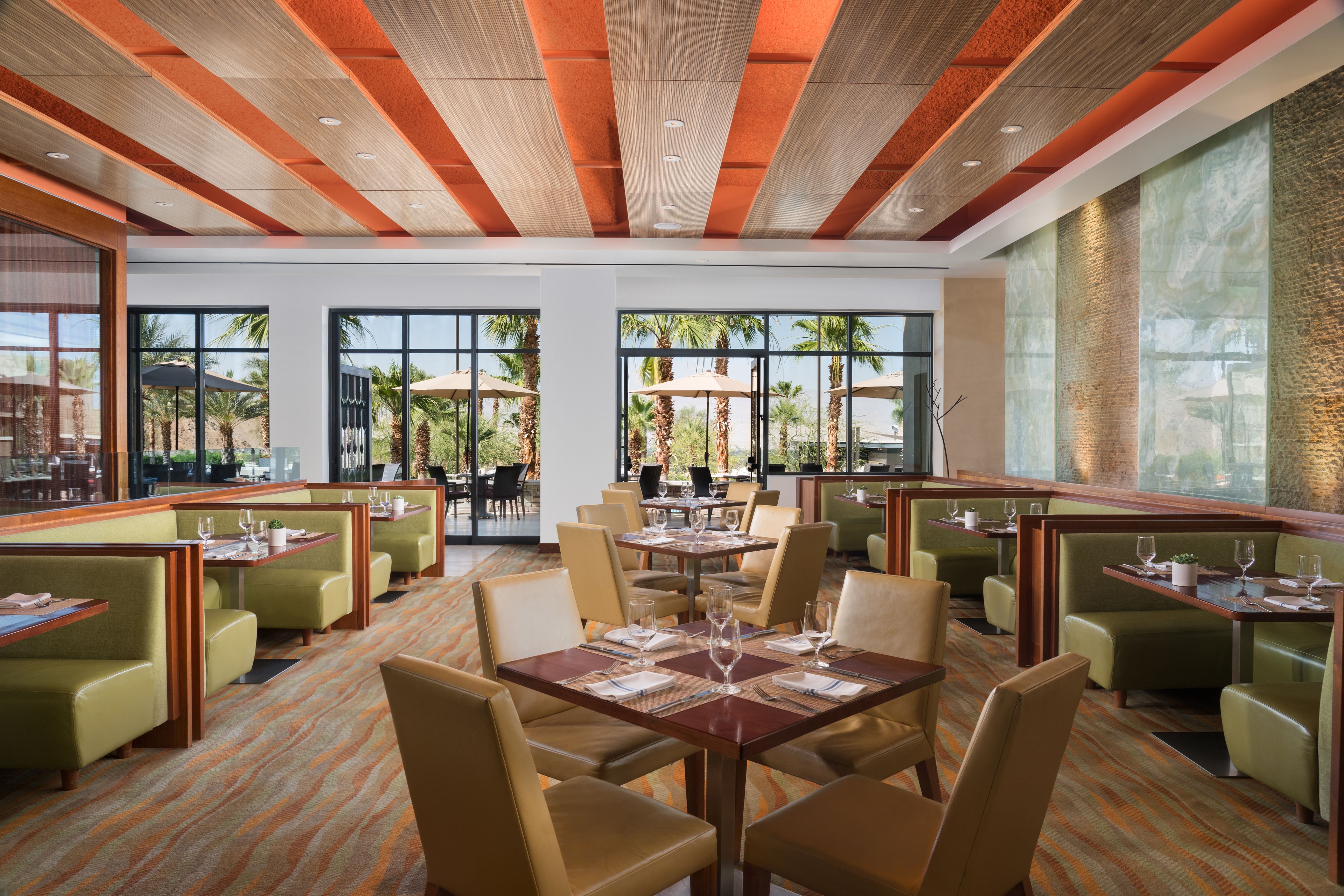 A spacious restaurant with high ceilings and large windows, offering views of palm trees and a clear sky.