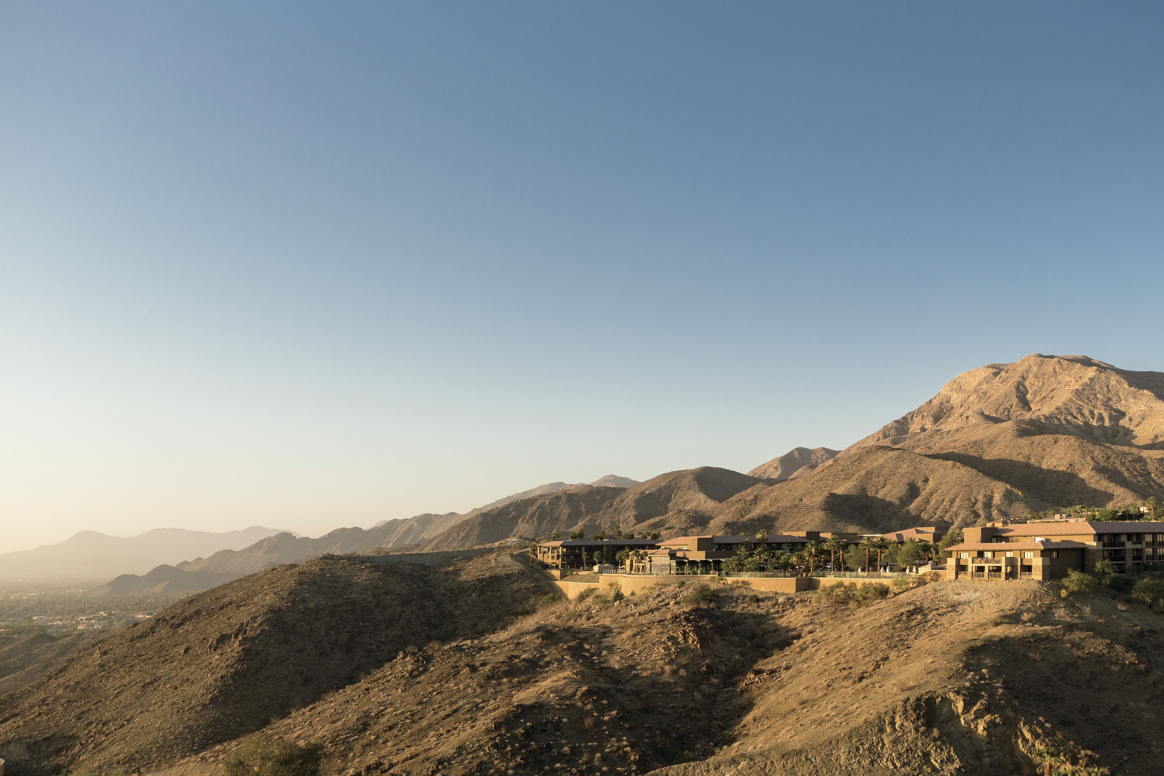Un resort en el desierto con varias construcciones, incluyendo un edificio principal del resort y casas de huéspedes más pequeñas, con montañas al fondo.