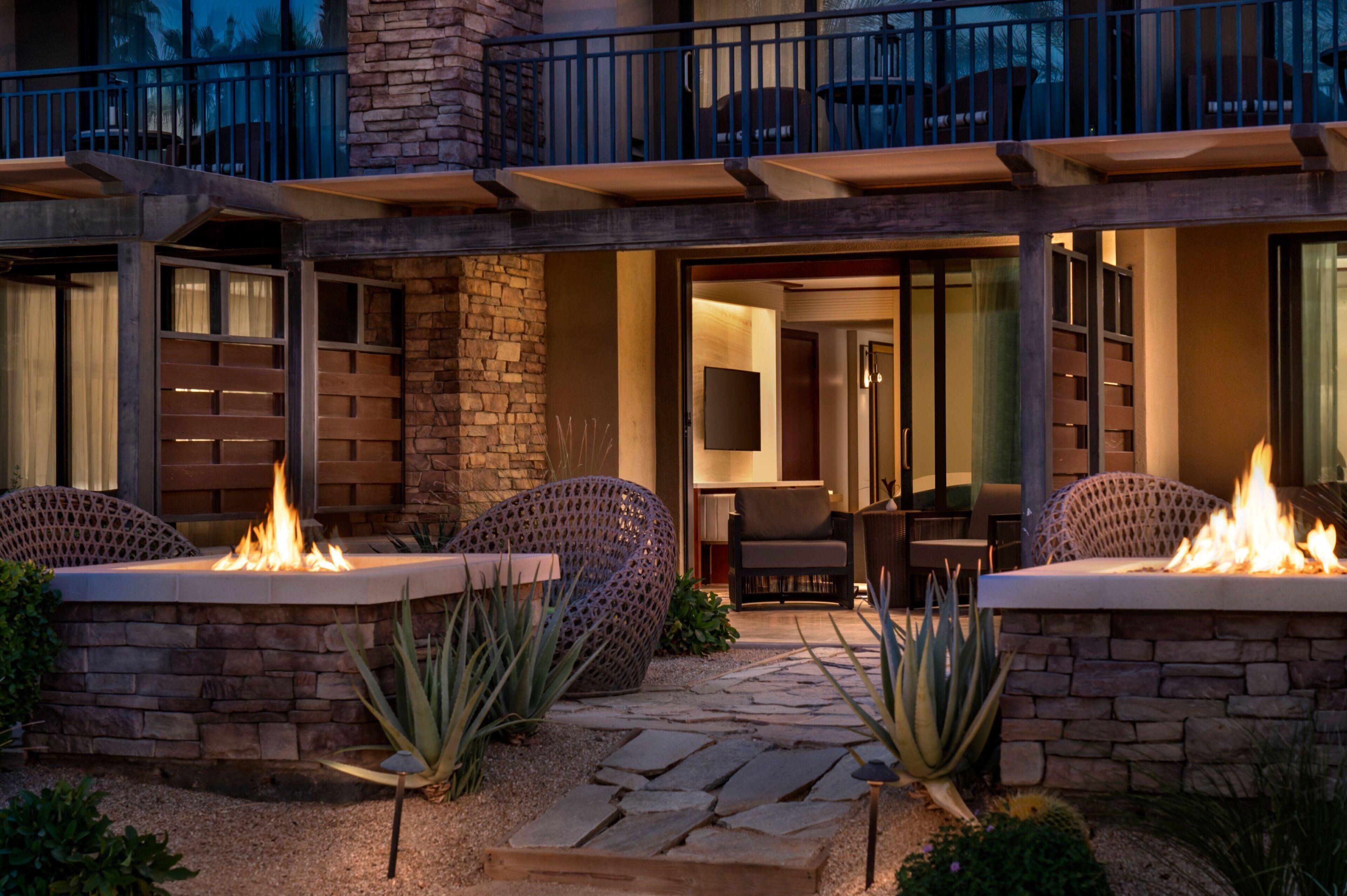 A modern outdoor patio with stone walls, two fire pits, and outdoor furniture.