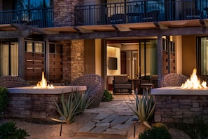 A modern outdoor patio with stone walls, two fire pits, and outdoor furniture.
