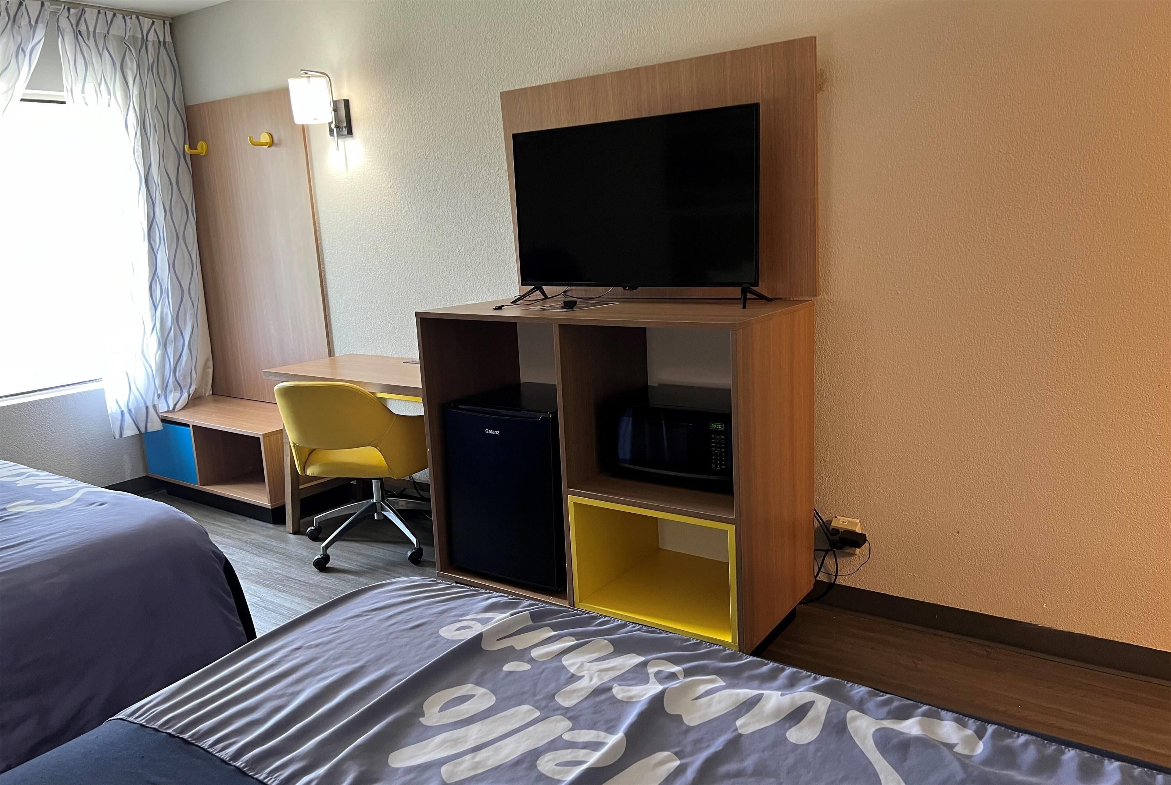 Ett hotellrum med en säng, ett skrivbord med en stol, en tv, ett minikylskåp och en mikrovågsugn.