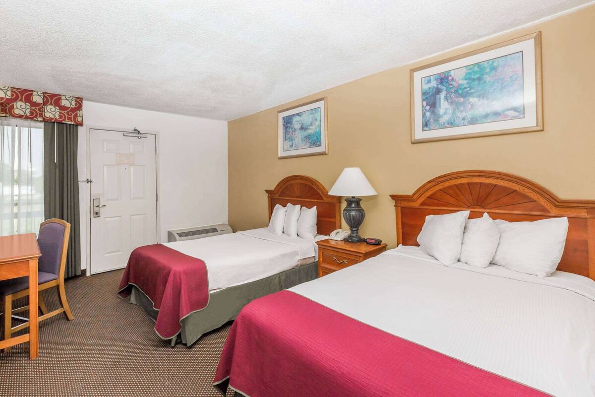 A hotel room with two beds, a desk, a chair, and a door.