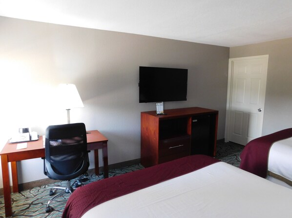 A hotel room with a bed, a desk with a chair, a television, and a door.