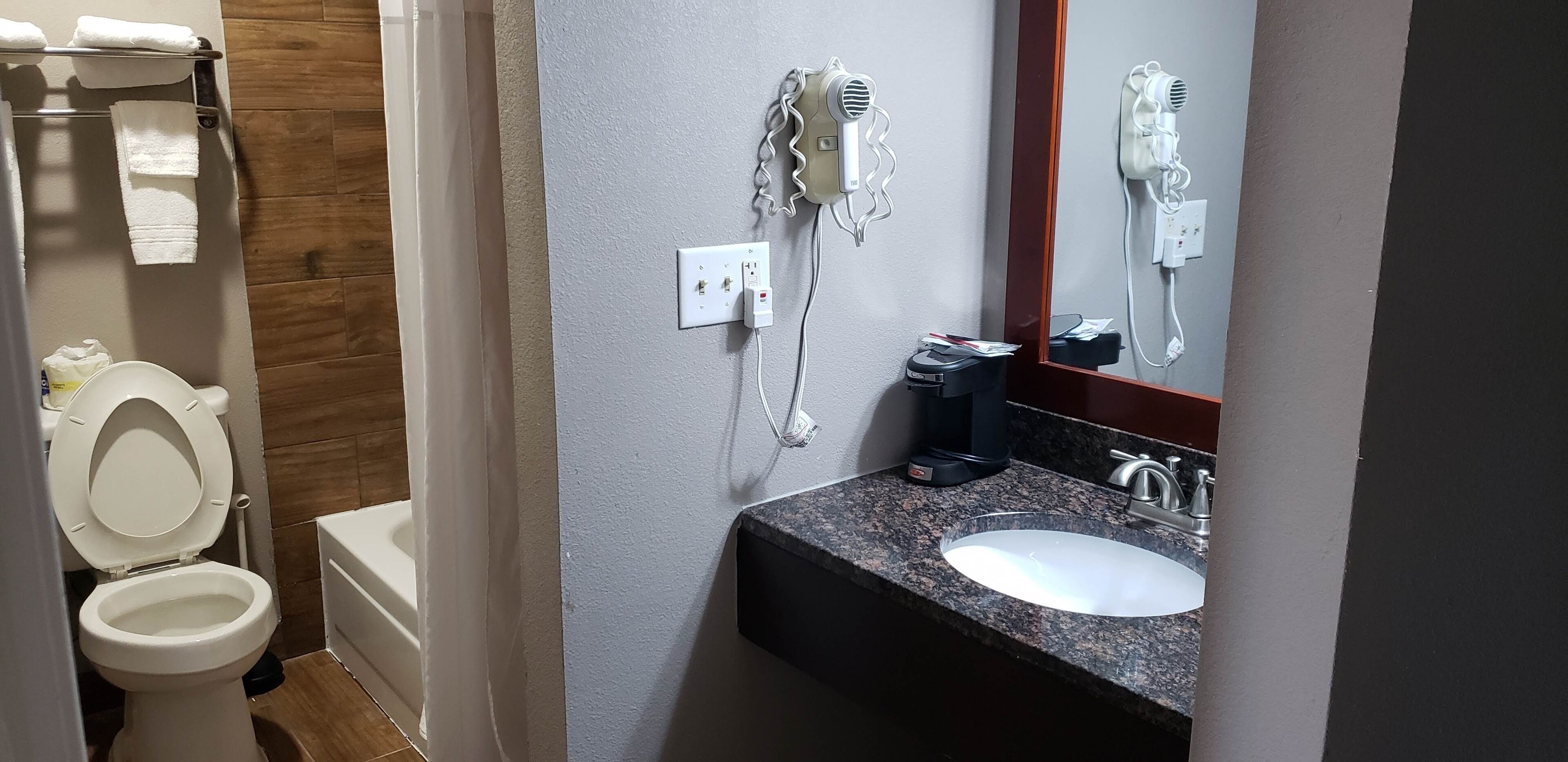 A bathroom with a white toilet, a sink with a granite countertop, and a hairdryer mounted on the wall.