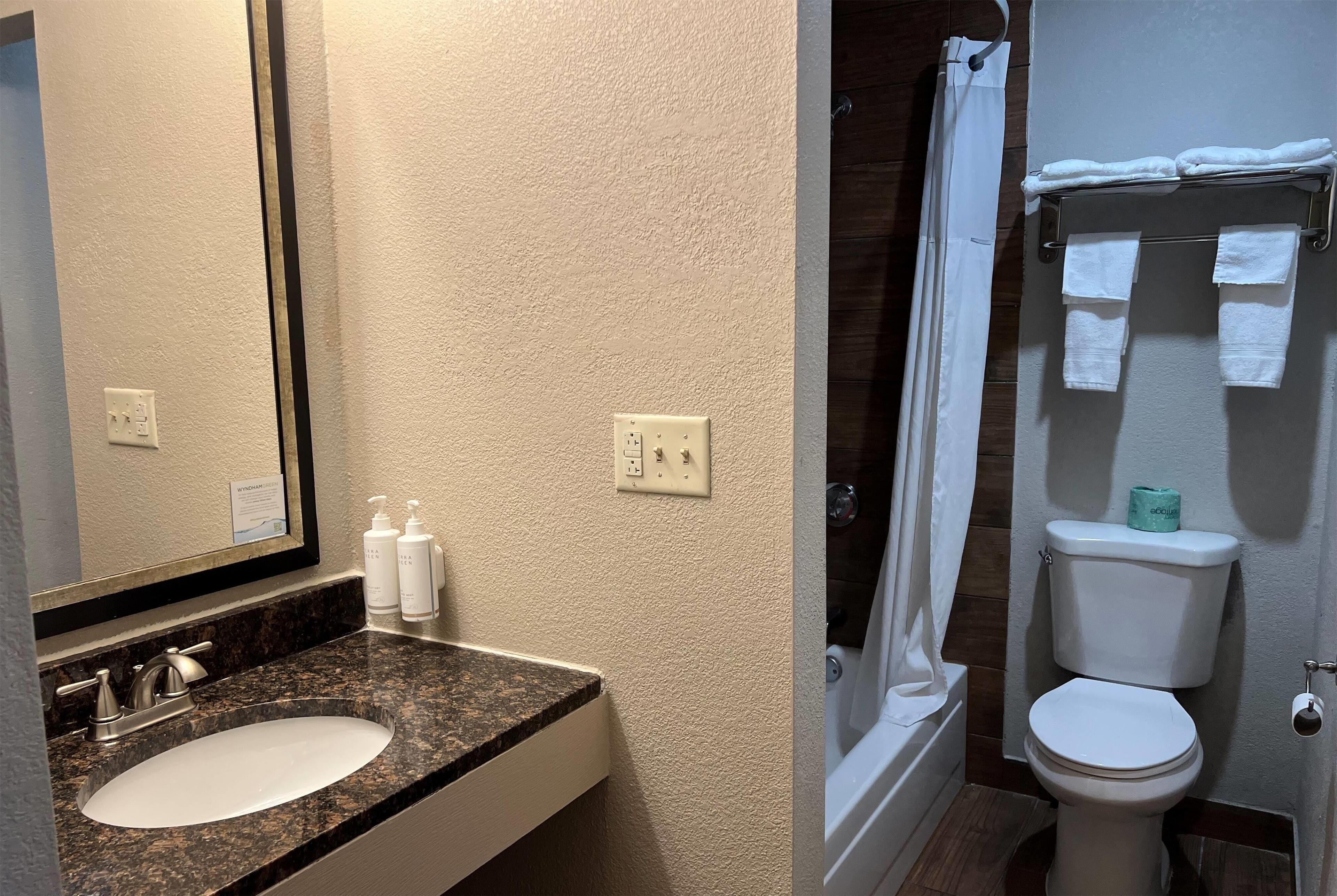 A bathroom with a granite countertop sink, a mirror, and a shower area with a white toilet and towel rack.