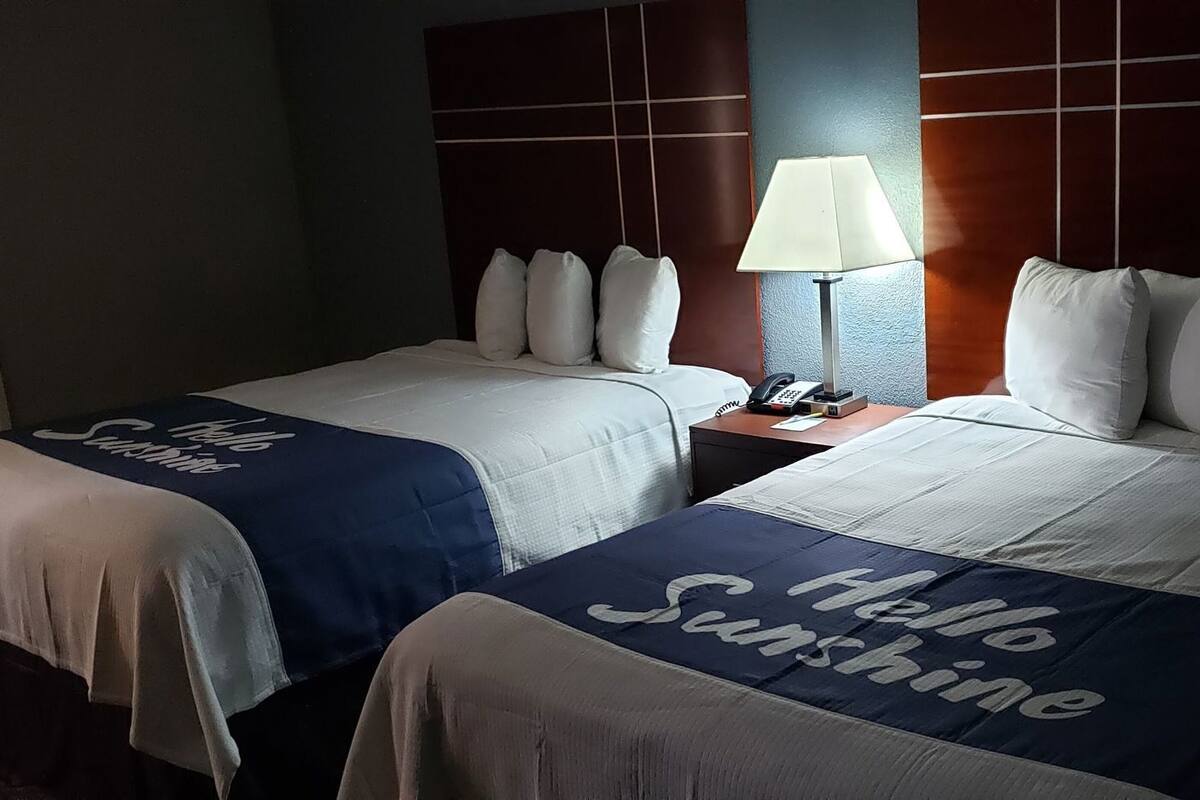 A hotel room with two beds, each with a 'Hello Sunshine' themed bedspread, a nightstand with a lamp, and a phone.