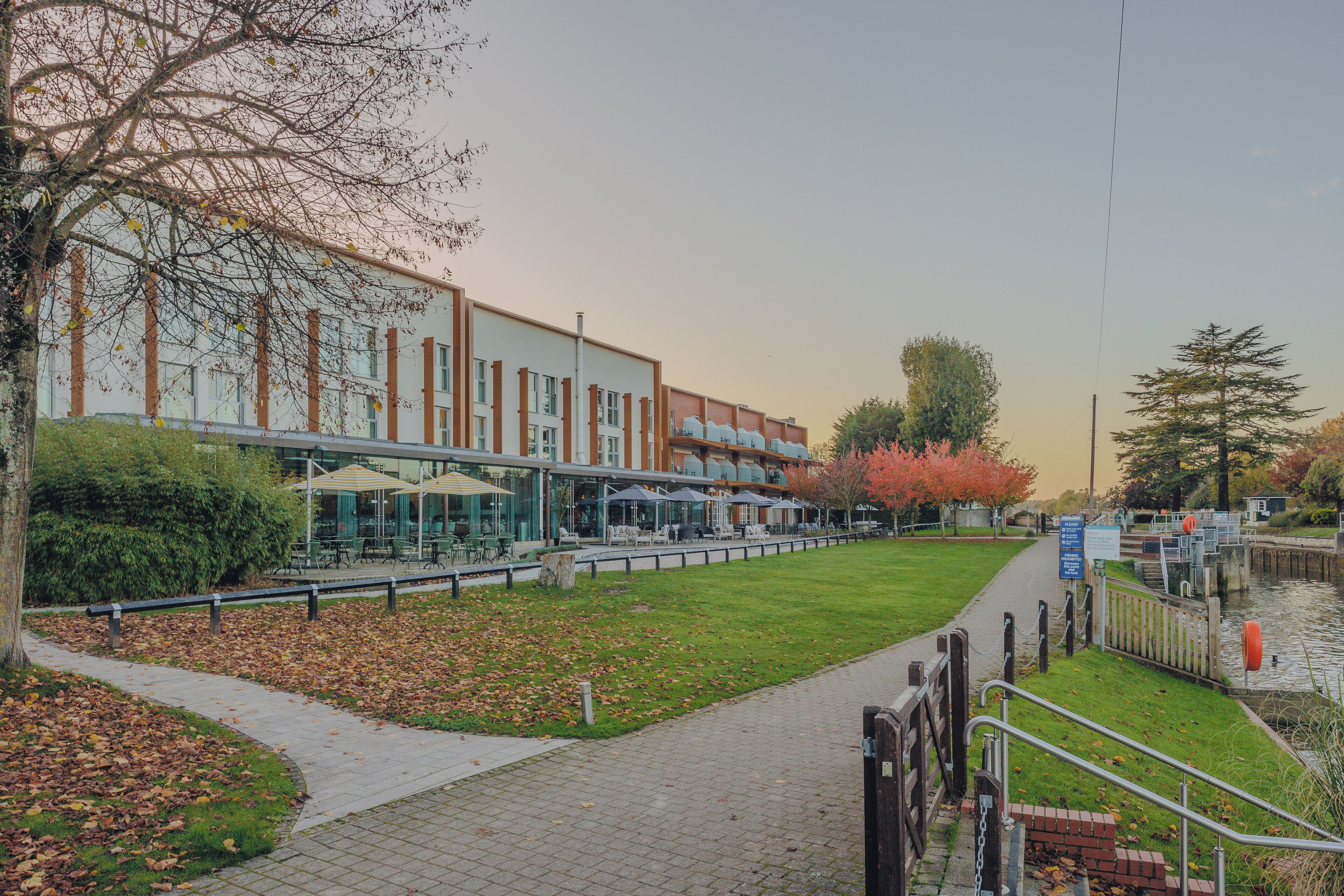A riverside walkway with a building featuring outdoor seating and a lock gate.