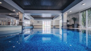 Una amplia piscina interior con suelo de baldosas, rodeada por un moderno hall con techos altos y grandes ventanales.