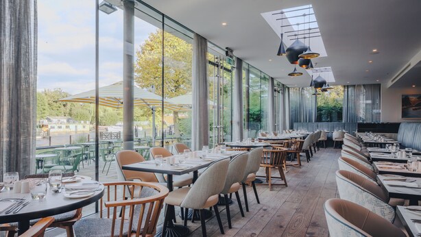 Un restaurante con amplios ventanales, mesas y sillas de madera.