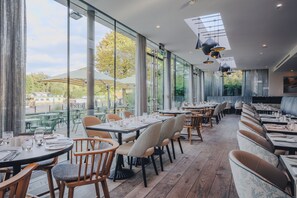 Un restaurante con amplios ventanales, mesas y sillas de madera.