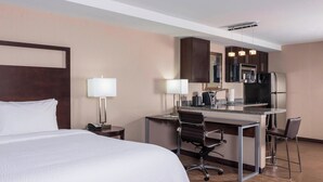 A hotel room with a bed, desk, chairs, and a kitchenette.