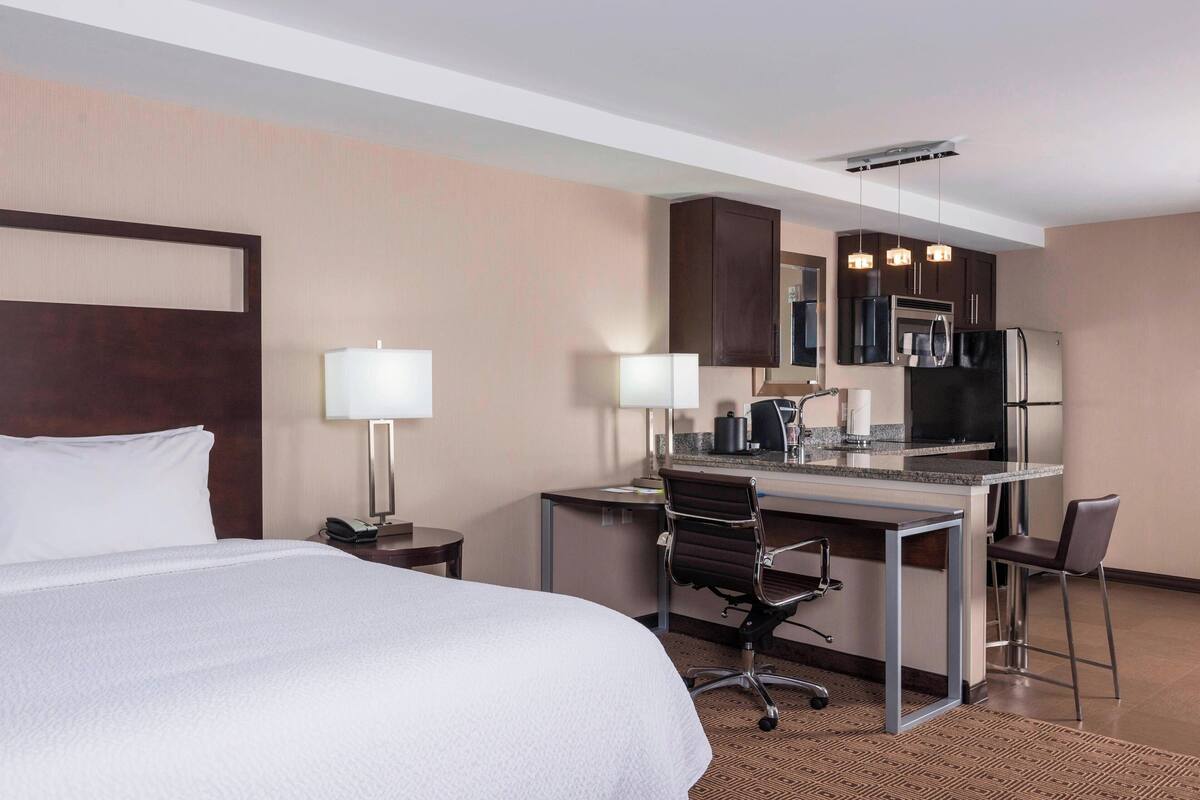 A hotel room with a bed, desk, chairs, and a kitchenette.