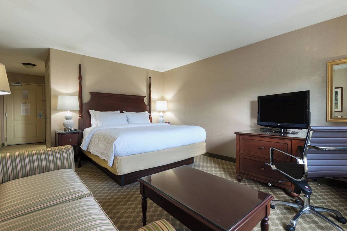 A hotel room with a bed, a television, a desk, a chair, and a lamp.