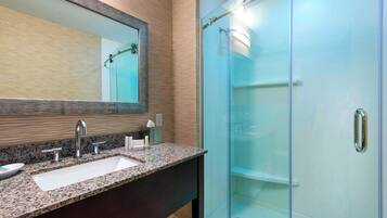A bathroom with a granite countertop sink, a large mirror, and a glass-enclosed shower.