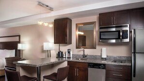A hotel kitchen with granite countertops, stainless steel appliances, and a bar area with stools.