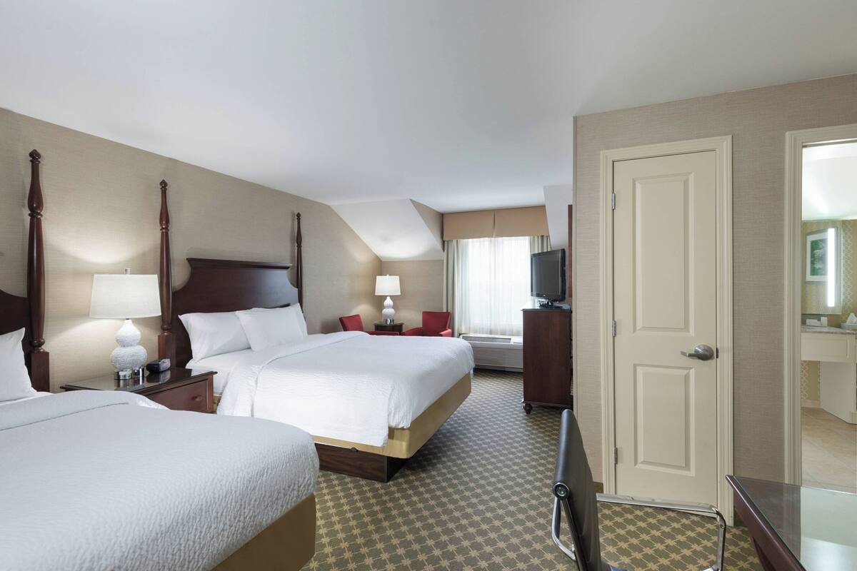 A hotel room with two beds, a television, a desk, and a mirror.