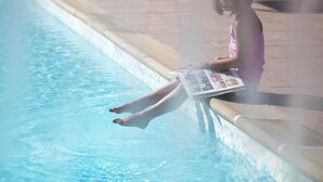 Una persona sentada junto a una piscina con una revista.