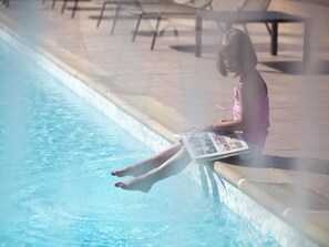 A person sitting by a pool with a magazine.