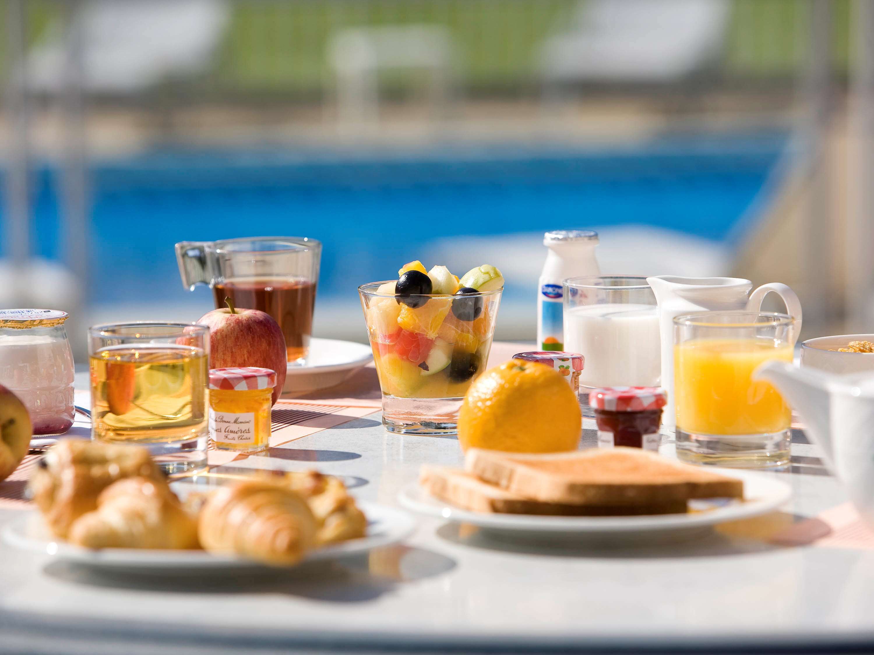 Et morgenbord med croissanter, frugtsalat, juice og mælk.