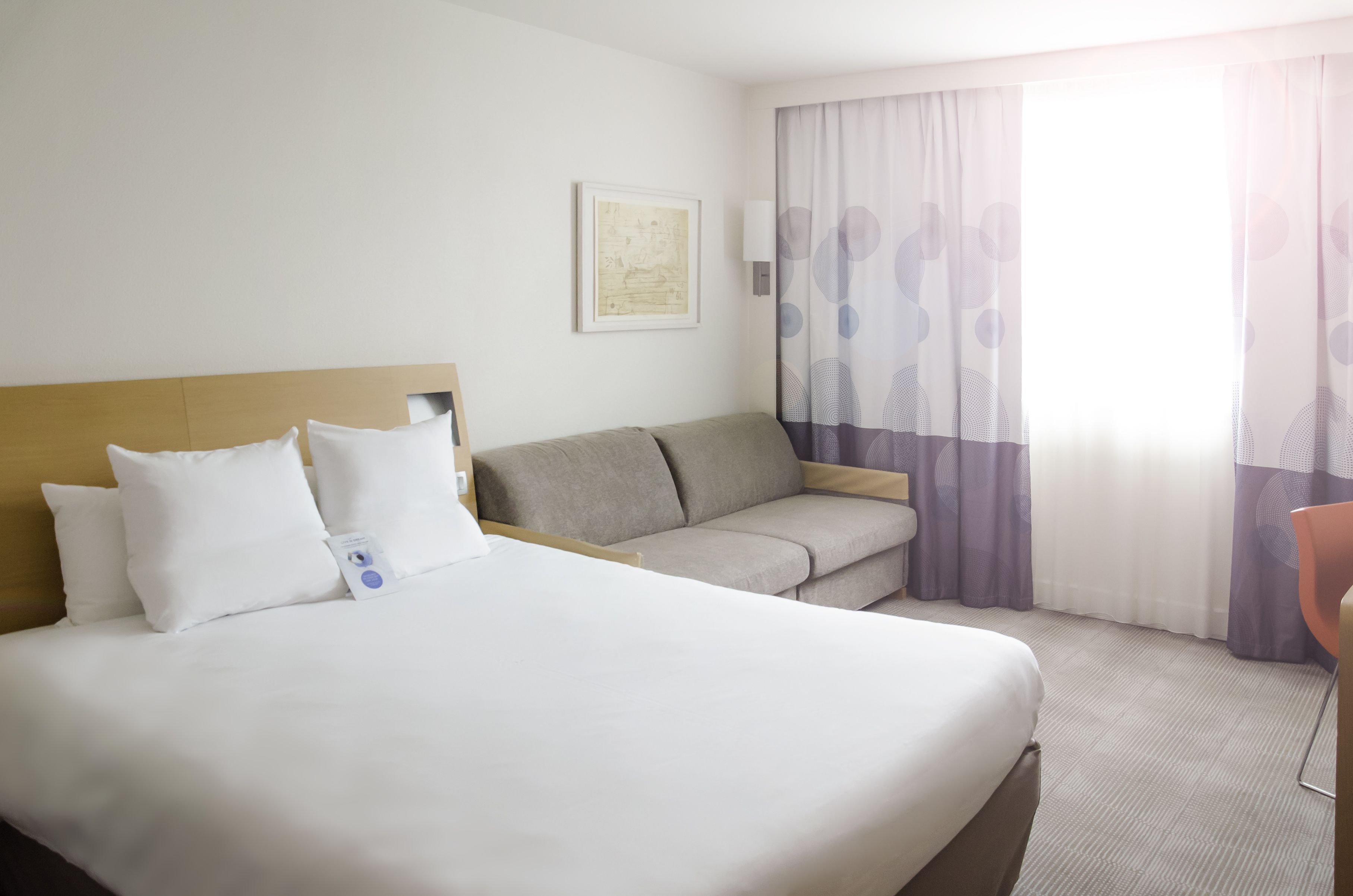 A hotel room with a large bed, a sofa, a small table, and a window with curtains.