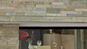 Un interior moderno con pared de piedra, una mesa de vidrio y una chimenea con llamas visibles.
