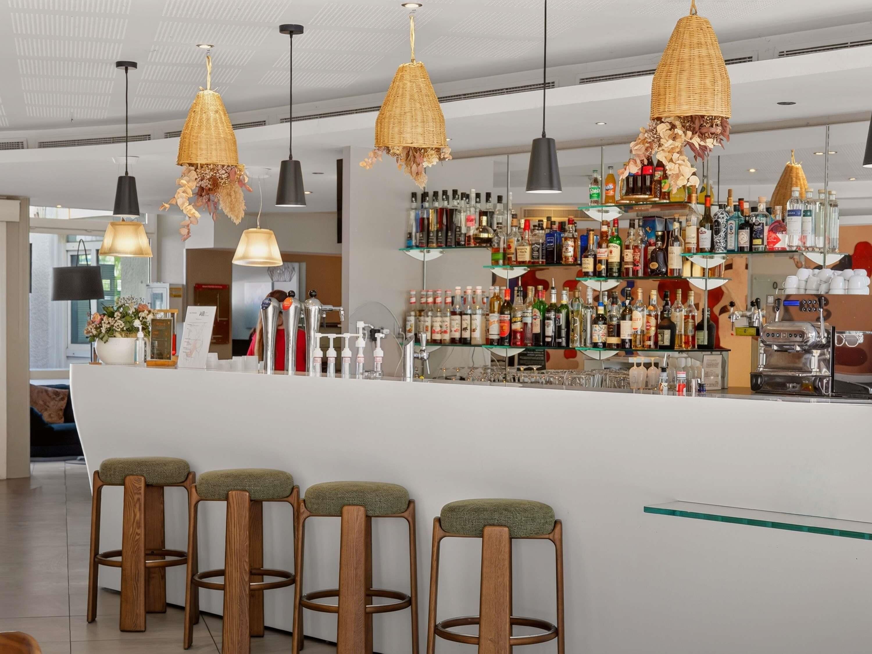 Un espace bar avec un comptoir, des tabourets, des lampes suspendues en osier et des étagères remplies de bouteilles.