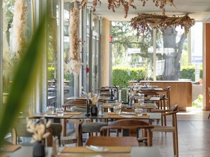 Un restaurante con mesas dispuestas para comer, ventanas amplias y decoraciones colgantes.