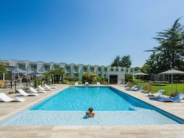 Una piscina con sillones de descanso y un edificio al fondo.