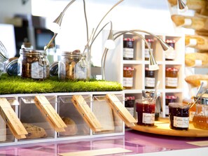 A display of baked goods and jars of preserves on a counter with a green grass-like surface. - Novotel Pau Pyrénées (Lescar)