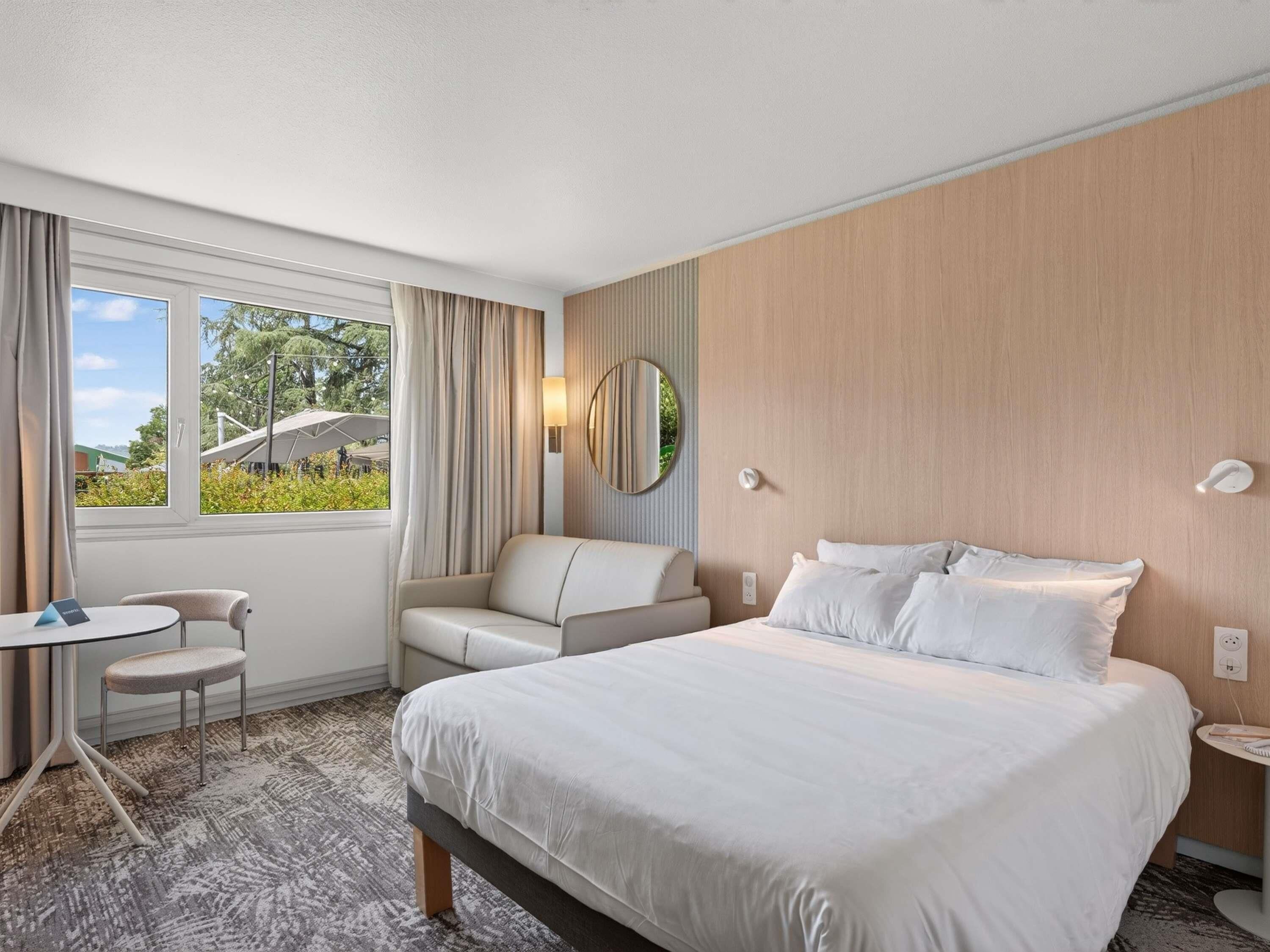 Une chambre d’hôtel avec un grand lit, un bureau, une chaise et une fenêtre avec des rideaux.
