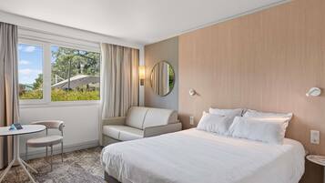 Une chambre d’hôtel avec un grand lit, un bureau, une chaise et une fenêtre avec des rideaux.