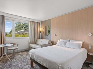 Habitación de hotel con una cama grande, un escritorio, una silla y un ventanal con cortinas.
