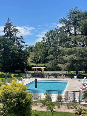 A swimming pool surrounded by a deck with lounge chairs, a covered seating area, and a fenced garden.