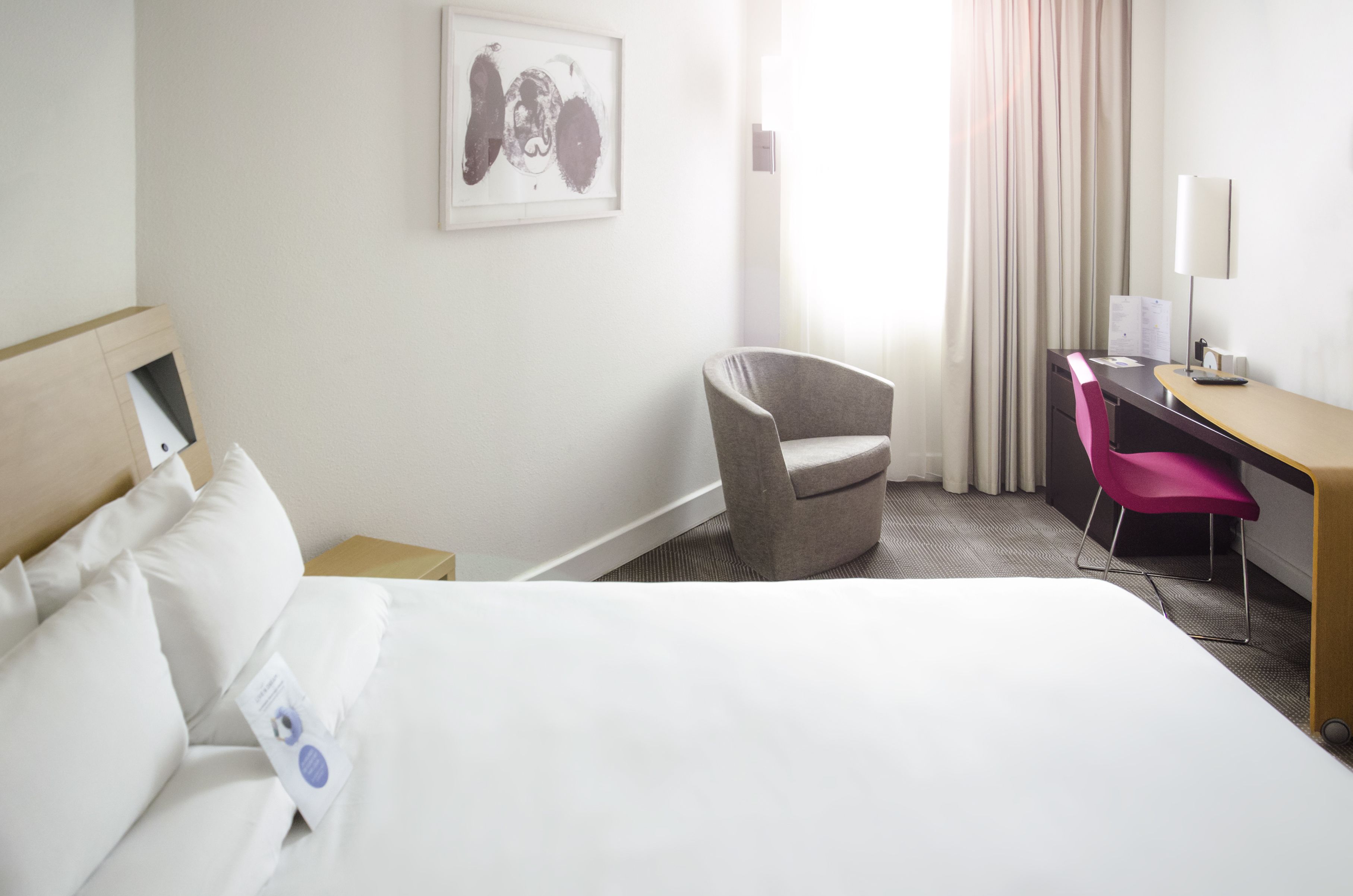 A hotel room with a bed, a desk, a chair, and a painting on the wall.